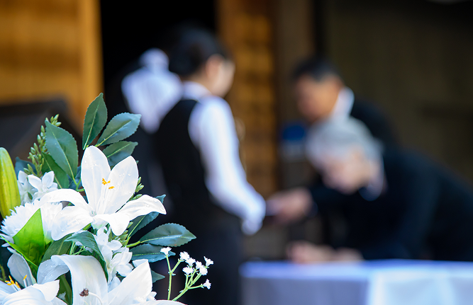 花の後ろで葬儀の受付をする様子の写真