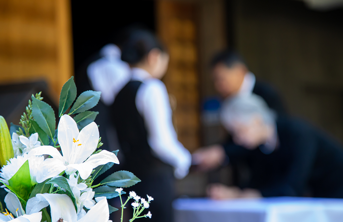 花の後ろで葬儀の受付をする様子の写真